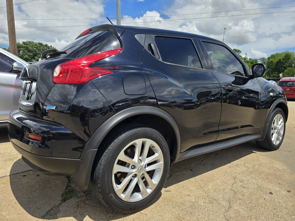Close-up of a black SUV's rear side and wheel in a parking lot under a bright sky.