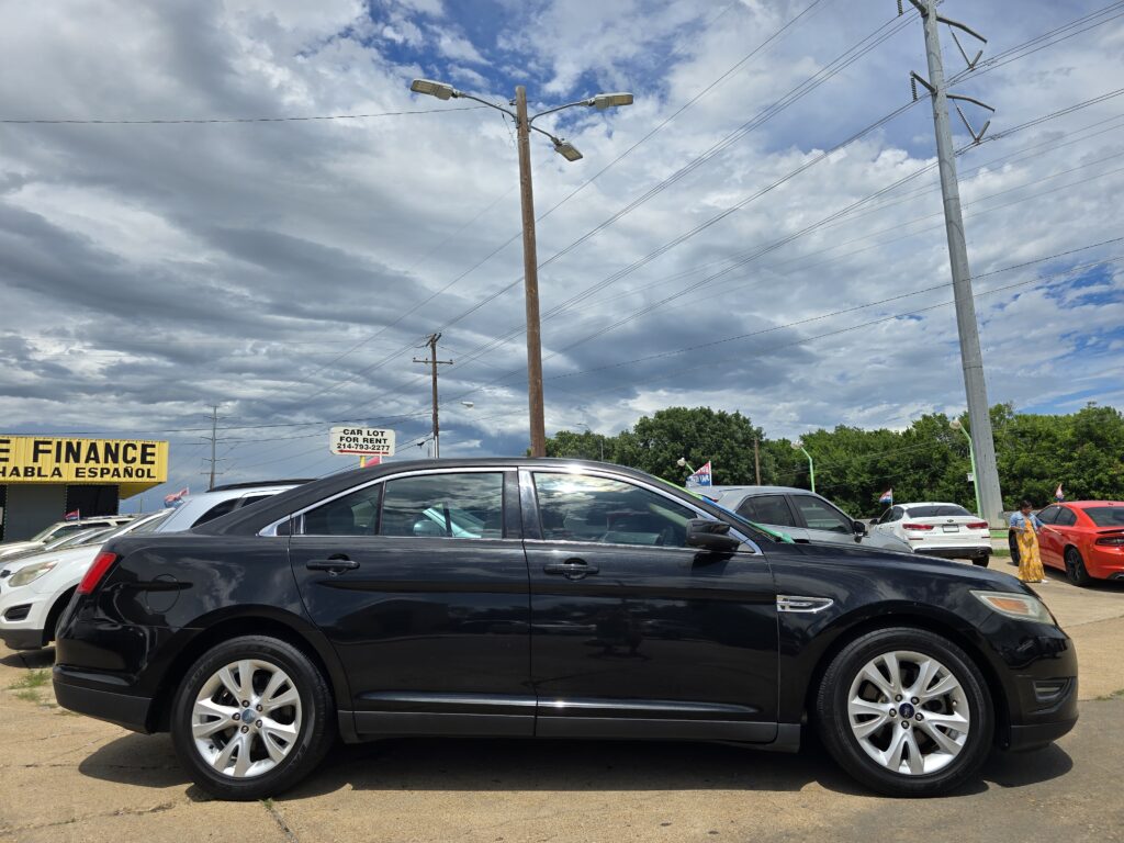 Row of dark-colored cars parked at a car dealership lot under a cloudy sky, with a yellow finance sign visible on the left.