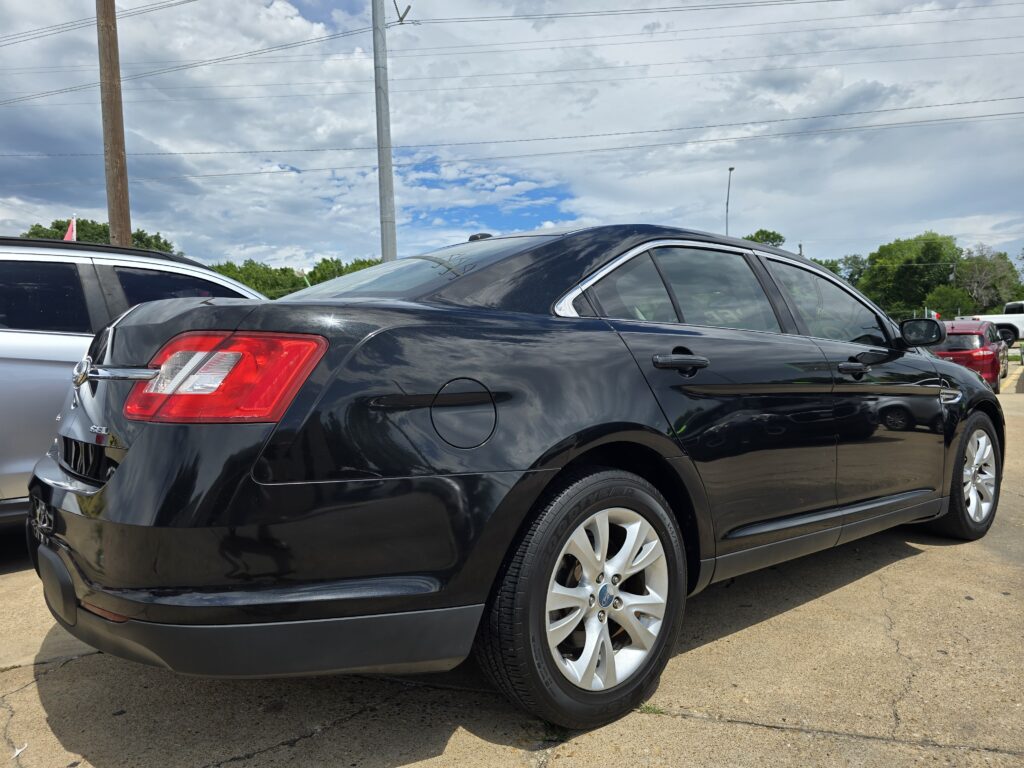 Black sedan parked in a lot with other vehicles, under a cloudy sky and power lines overhead.