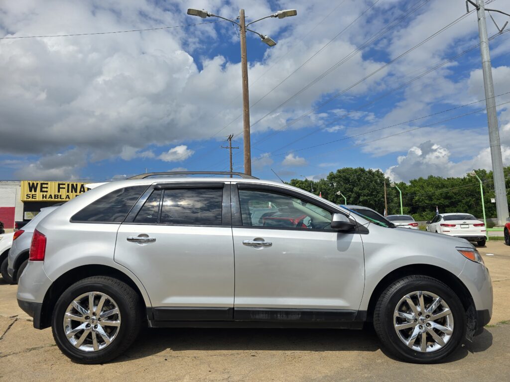 Silver SUV in foreground parked in a dealership lot with other cars, power lines, and a cloudy blue sky behind.