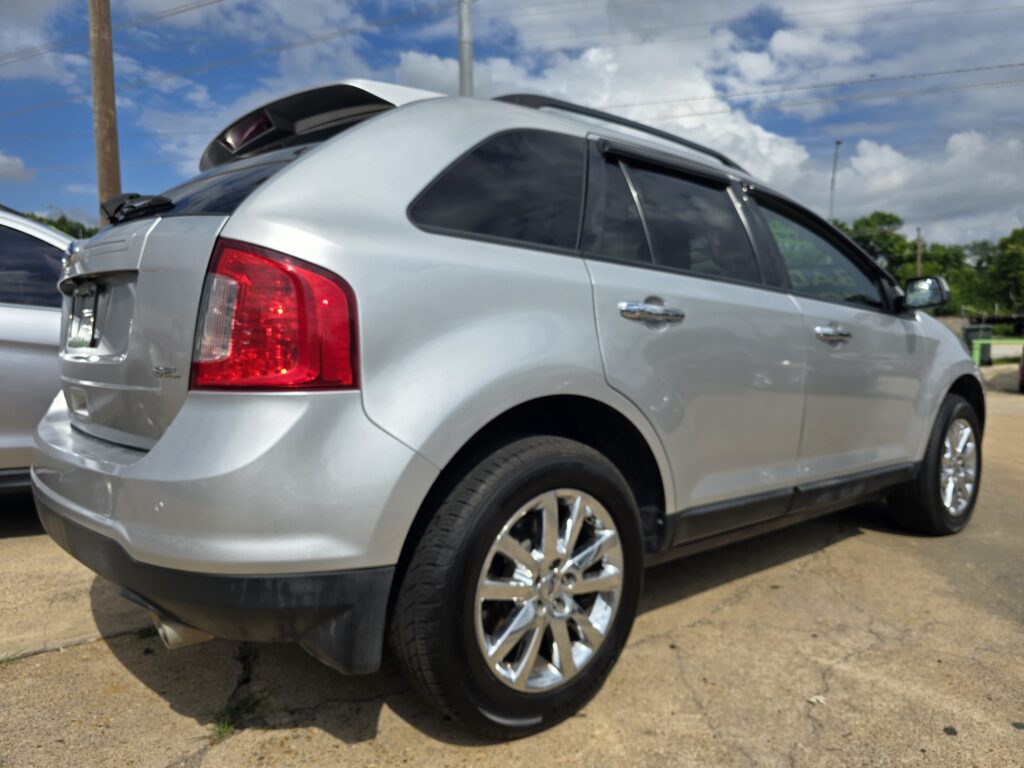 Rear quarter view of a silver SUV with tinted windows, chrome wheels, parked on a sunny street.