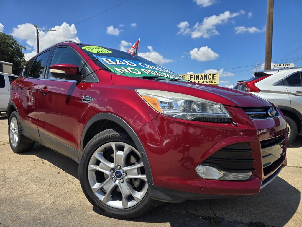 Close-up of a red Ford SUV on a dealership lot with a bold sale sign on the windshield reading 'BAD CREDIT NO PROBLEM' against a bright blue sky.