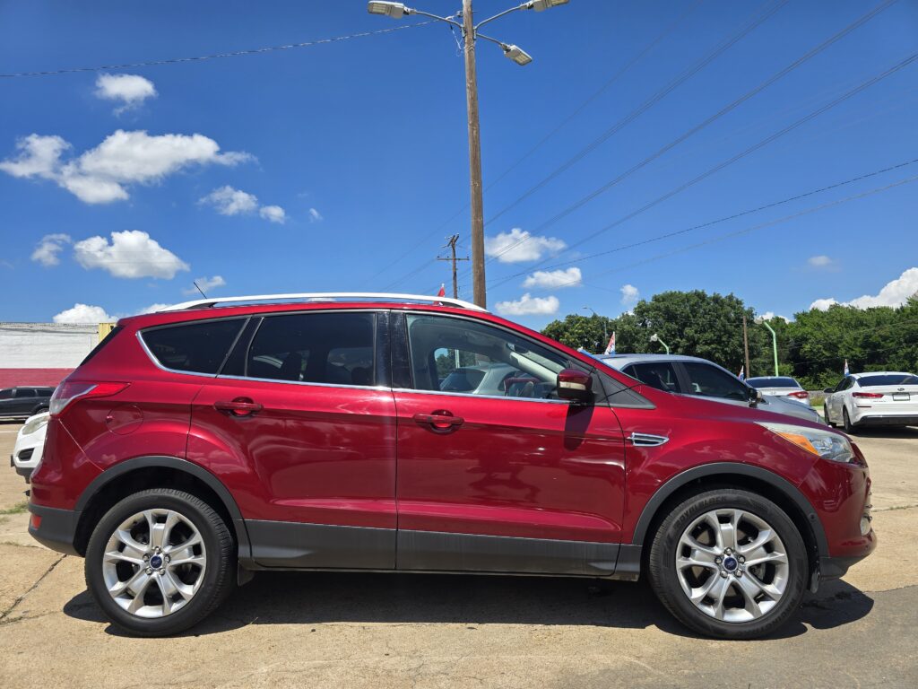 Close-up side view of a red SUV parked in a lot on a sunny day, with a blue sky and utility poles in the background.