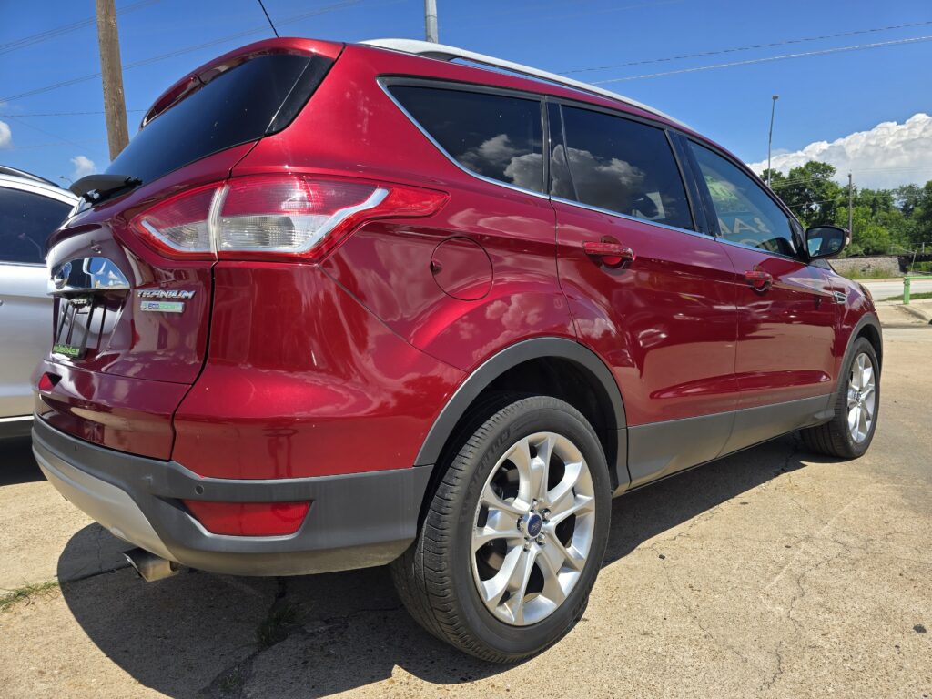 Rear three-quarter view of a red Ford SUV parked outdoors, showing taillight, gas cap, and alloy wheel on a sunny day