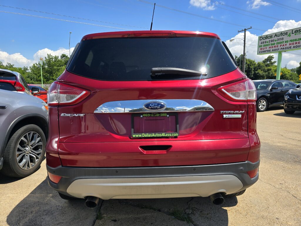 Rear view of a red Ford Escape Titanium in a dealership lot, plenty of other cars nearby and a Dallas Autos 4 Less sign visible in the background.