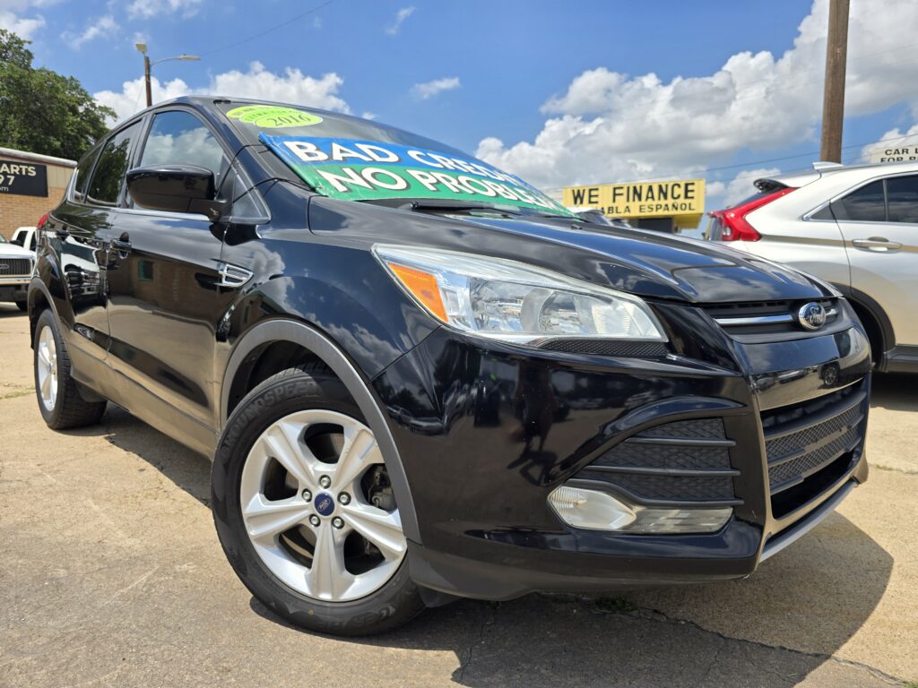 Front-left view of a black SUV with a green windshield sign reading 'BAD CREDIT NO PROBLEM' at a car lot; dealership signs in the background.