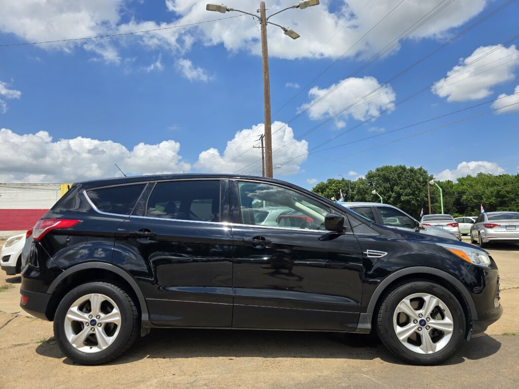 Black SUV parked in a parking lot with a tall wooden utility pole and a bright blue sky with white clouds in the background.