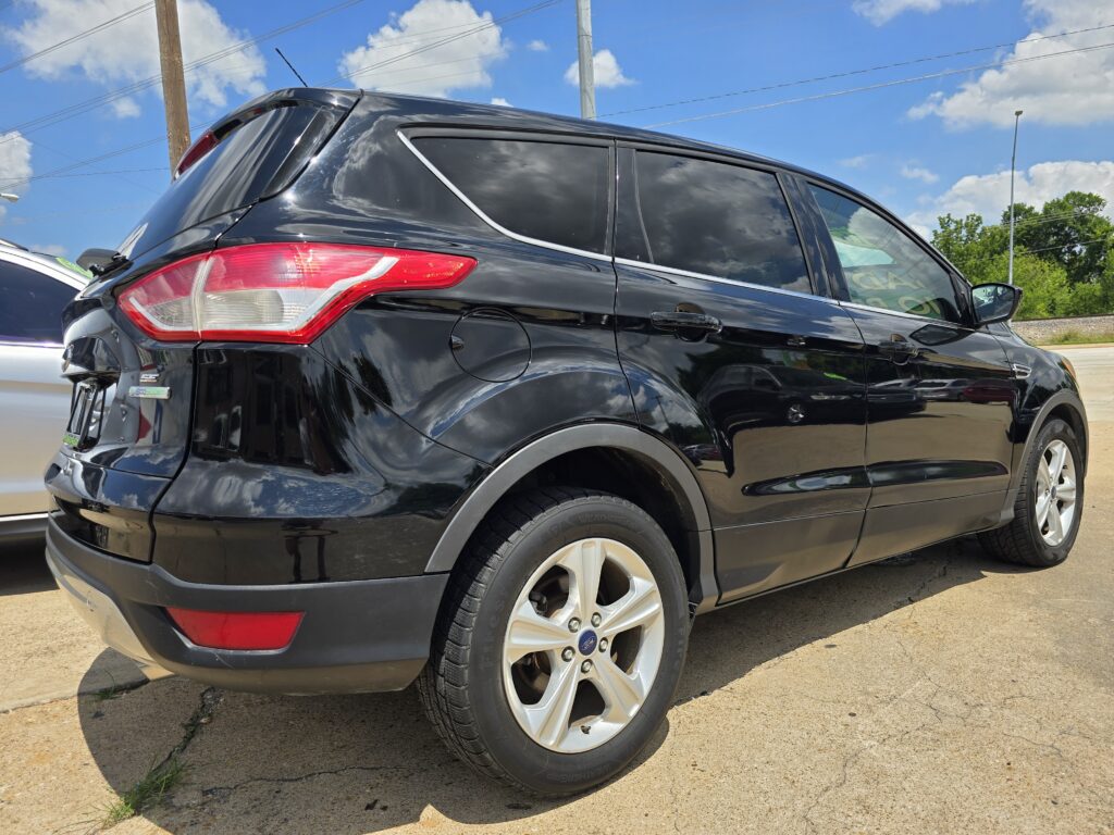 Black SUV parked on a sunny day, showing rear and side with tinted windows and alloy wheels under a blue sky with clouds.