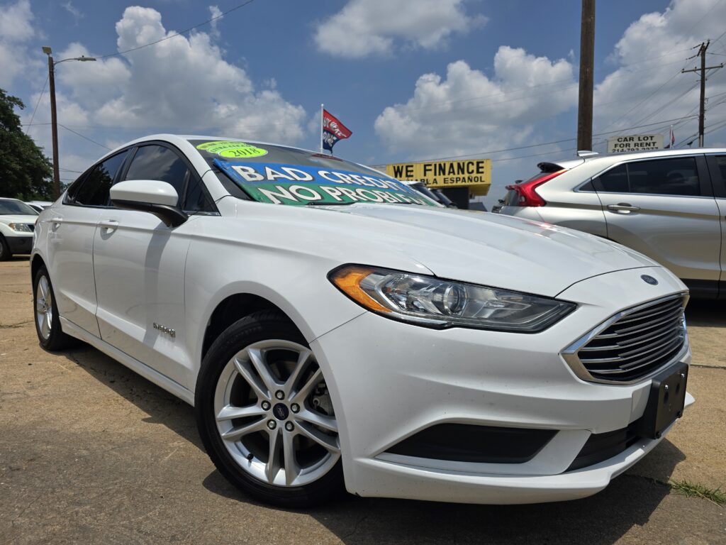 White Ford sedan at a used-car lot with a bright windshield banner reading BAD CREDIT NO PROBLEM against a blue sky.