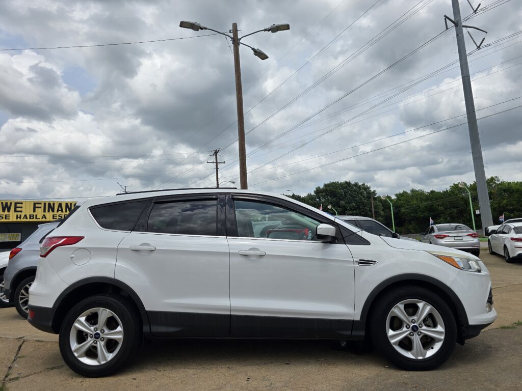 Line of white SUVs parked in a dealership lot under a cloudy sky with power lines overhead