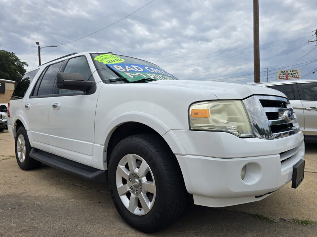 White SUV on a dealership lot with bright sale signs in the windshield and a cloudy sky above