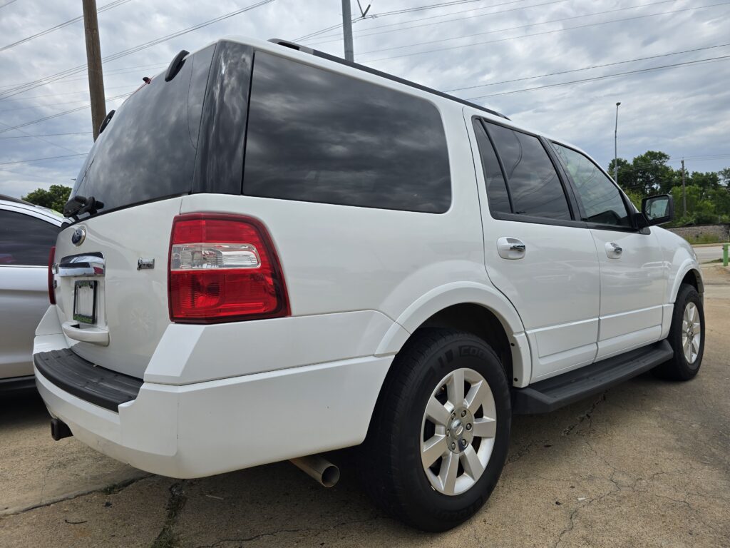 White SUV parked in a lot, seen from the rear-left side with tinted windows and red tail light.