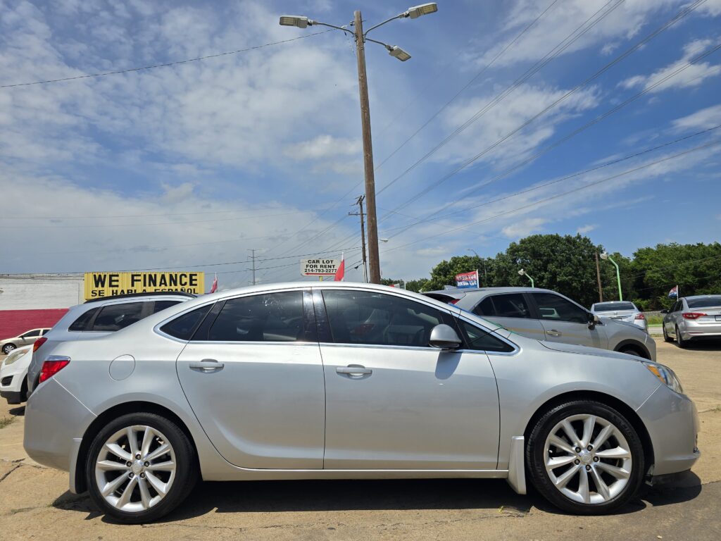 Silver car in a parking lot with a large yellow 'WE FINANCE' sign in the background under a blue sky with wispy clouds and power lines overhead.