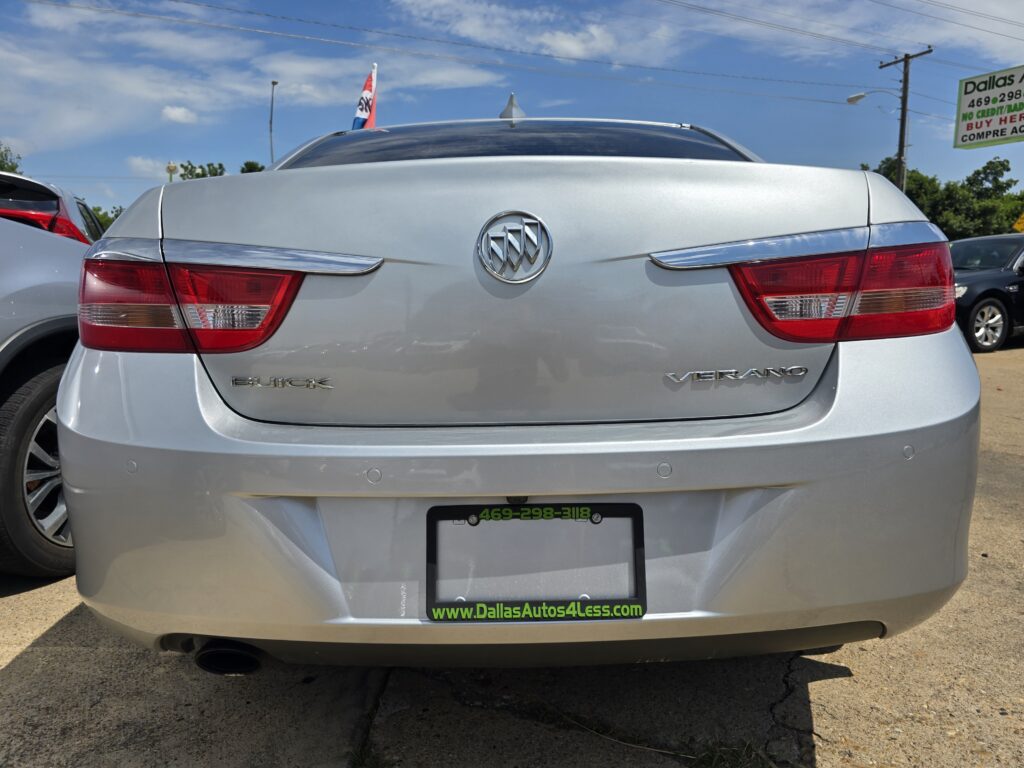 Rear view of a silver Buick Verano on a car lot, showing the Buick emblem and taillights in focus.