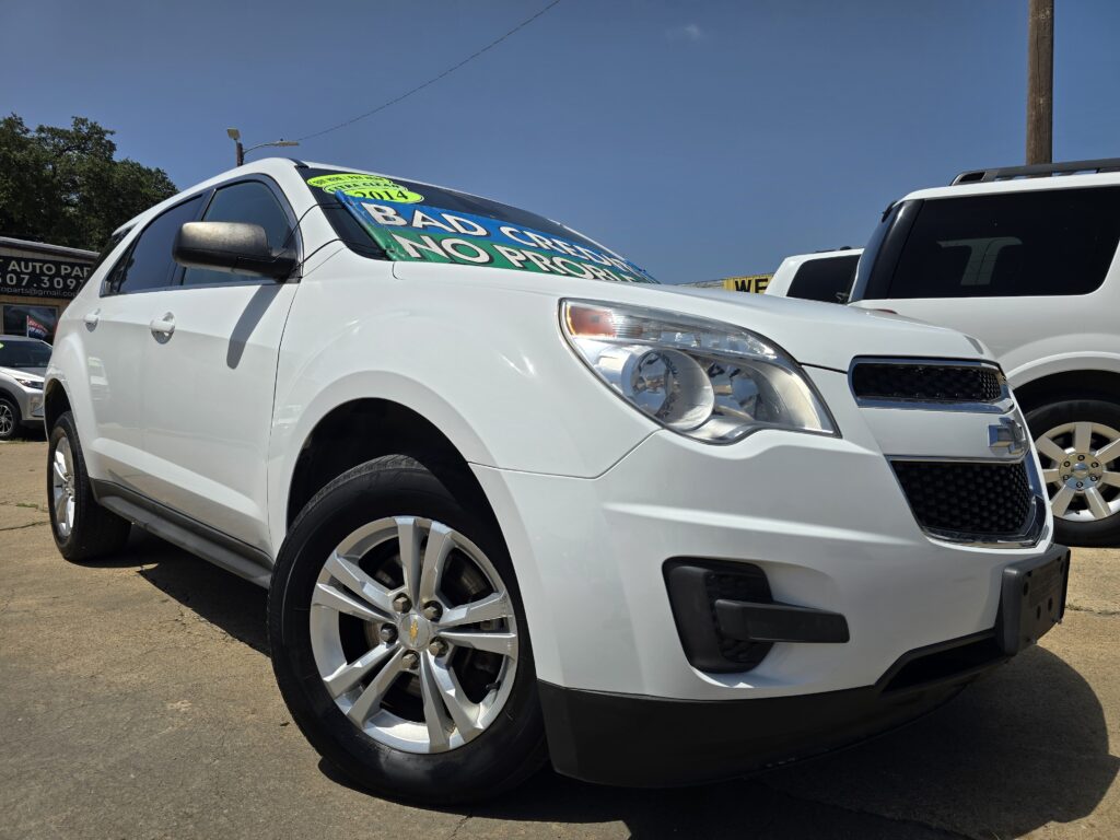 White SUV in a car dealership lot with a bright green sale banner on the windshield, flanked by other vehicles under a blue sky.
