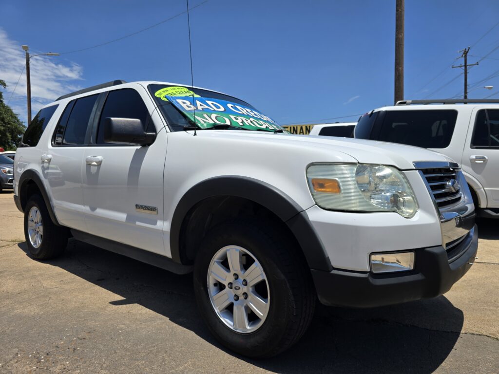 White SUV in a dealership lot with a large green and blue sale sign on the windshield reading 'BAD CREDIT' (used cars available).