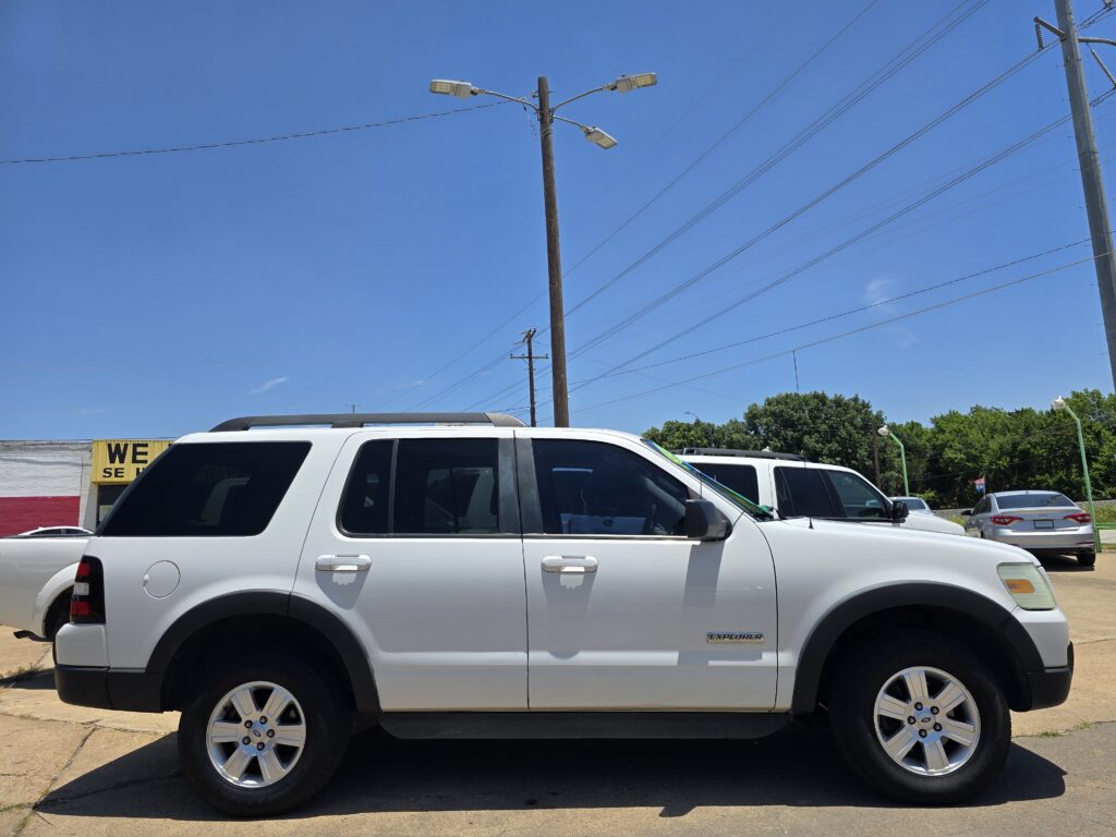 White SUV parked in a lot under a clear blue sky with power lines overhead in the background.