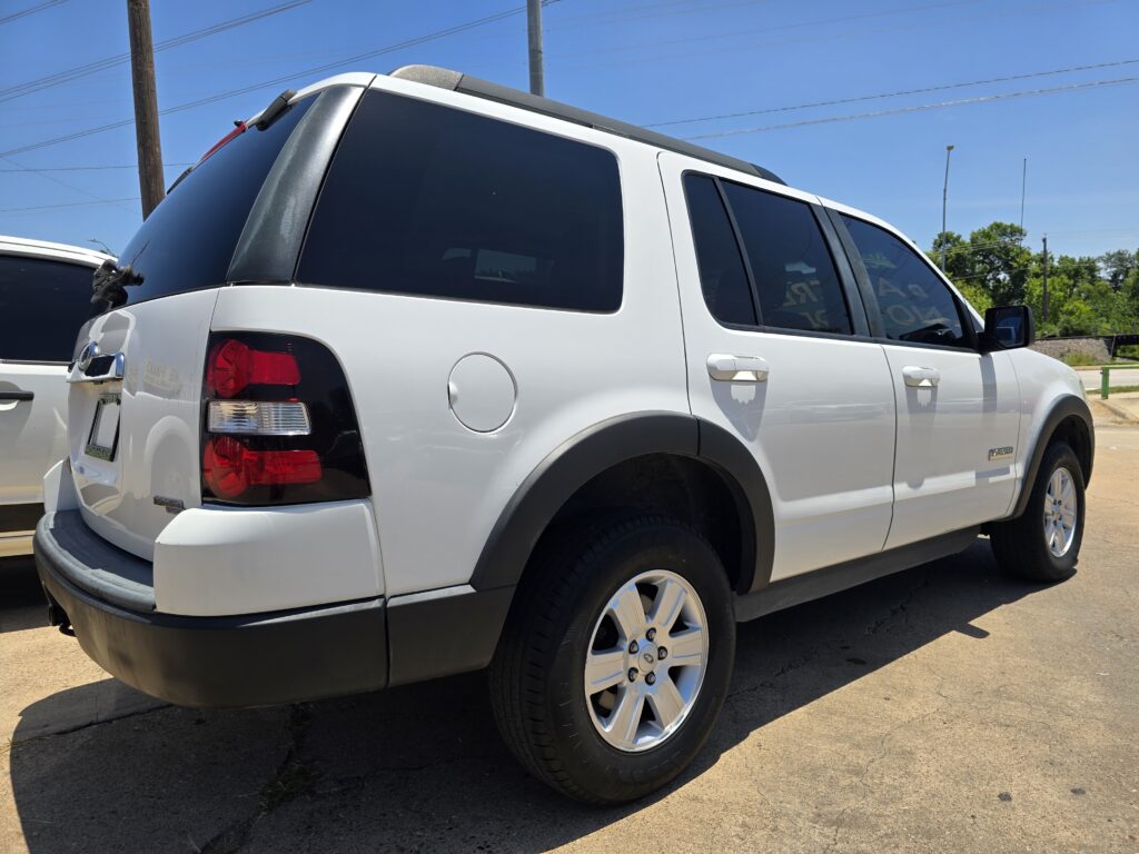 Rear three-quarter view of a white SUV with tinted windows and roof rails parked on a sunny day in a lot.