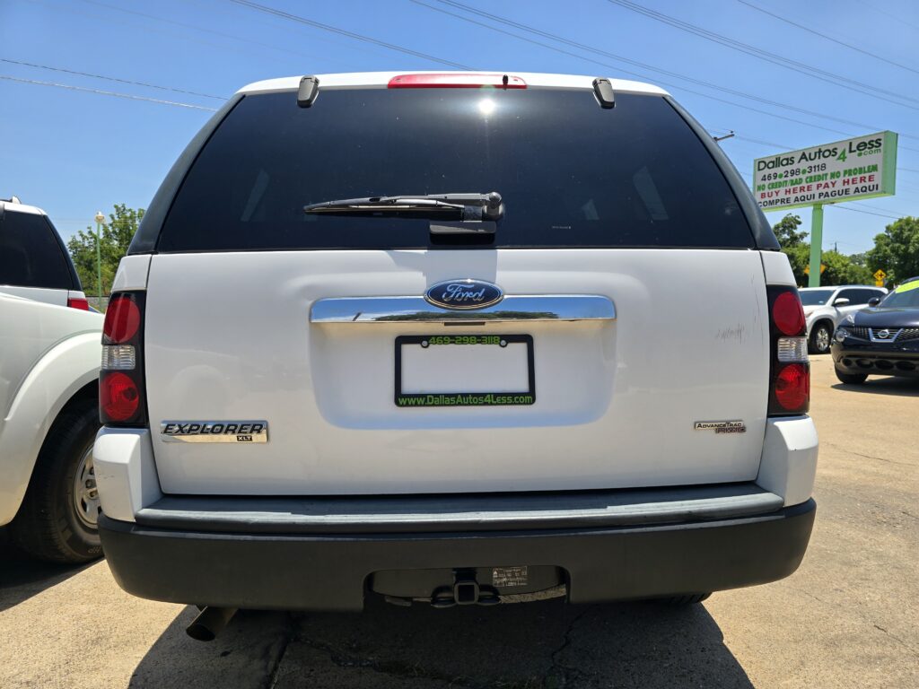 White Ford Explorer XLT rear view in a car dealership lot with a Dallas Autos 4 Less sign in the background on the right.