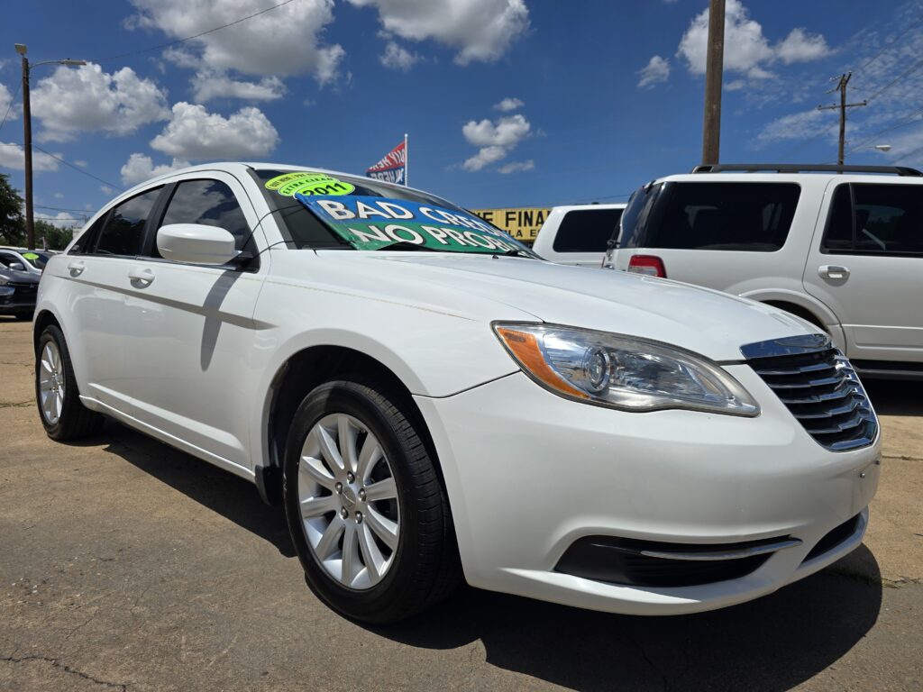 White sedan in a dealership lot with large green and yellow signs on the windshield reading 'BAD CREDIT NO PROBLEM'.