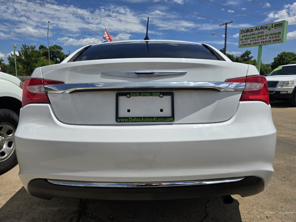 Rear view of a white car at a used-car lot; dealership sign in the background reads Dallas Autos 4 Less.