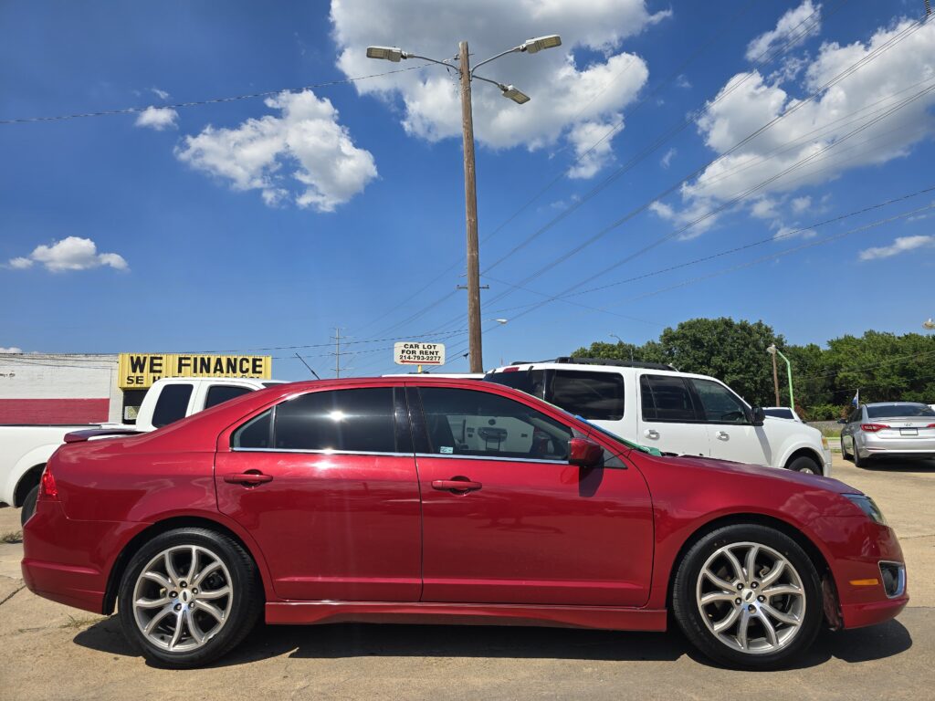 Red sedan in the foreground at a car dealership lot, with a bold yellow 'WE FINANCE' sign in the background against a clear blue sky.