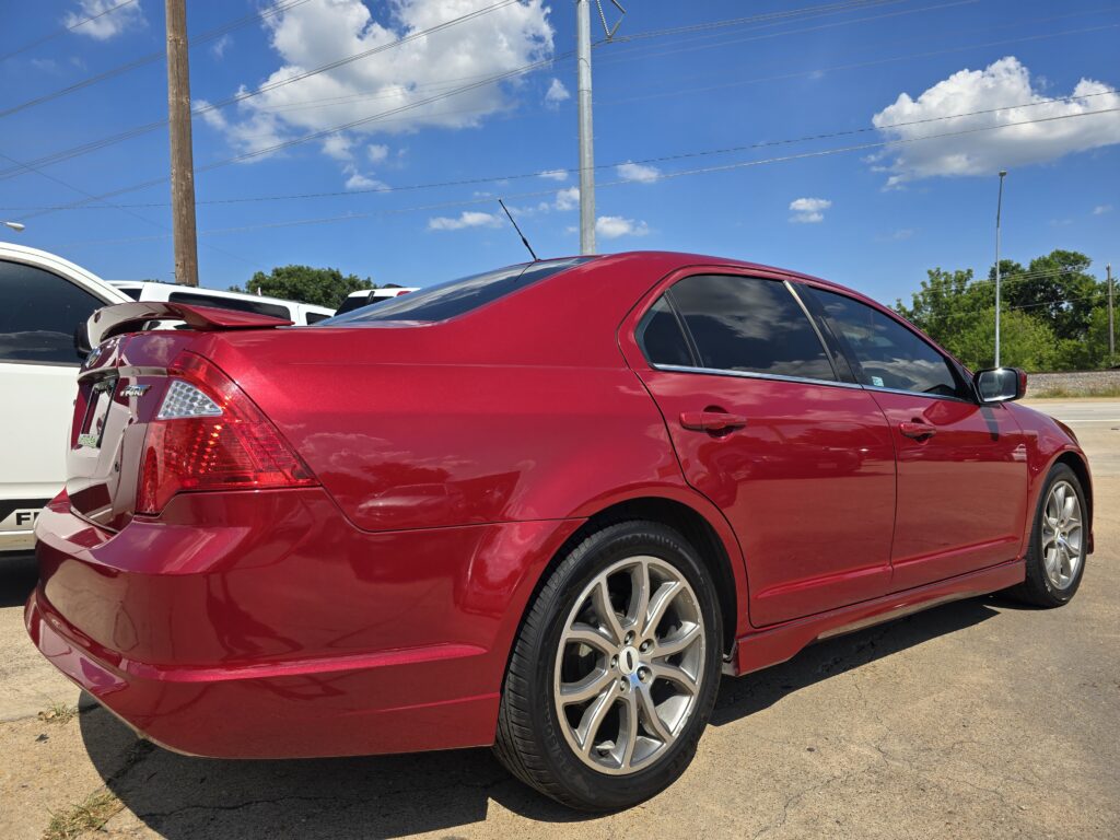 Close-up of a shiny red sedan parked in a lot with a white SUV behind and a blue sky above.