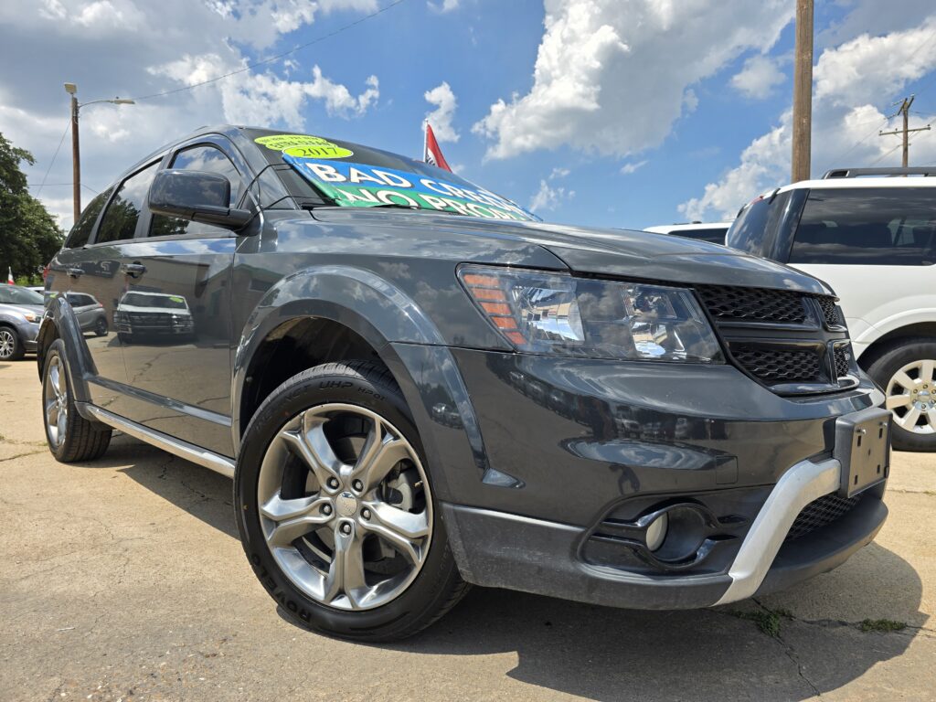 Gray SUV in a car lot with large colorful sale banners over the windshield, blue sky and clouds in the background.
