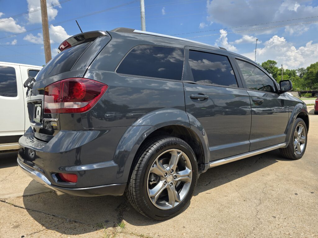 Side view of a dark gray SUV with tinted windows, parked on a sunny day beside a white vehicle, under a blue sky with clouds and utility poles in the background.