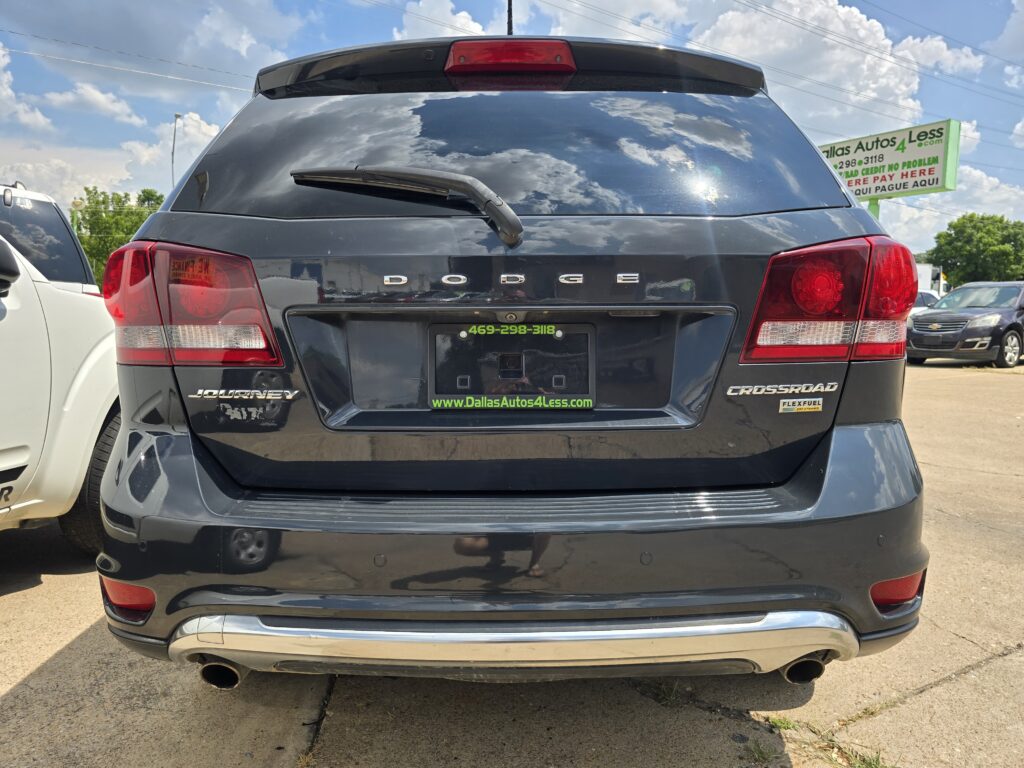 Rear view of a black Dodge Journey Crossroad SUV with red taillights and a rear windshield wiper in a dealership lot. The plate area shows green dealership text.