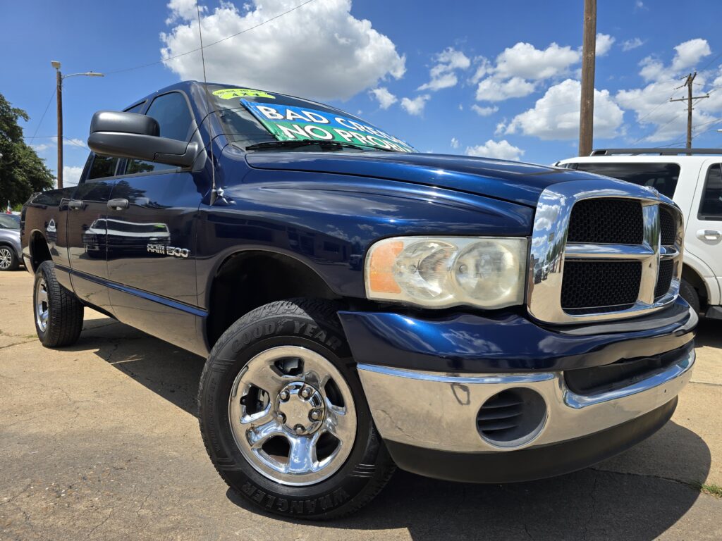 Blue Ram 1500 pickup at a dealership with a windshield banner reading 'Bad Credit? No Problem' on a sunny day.