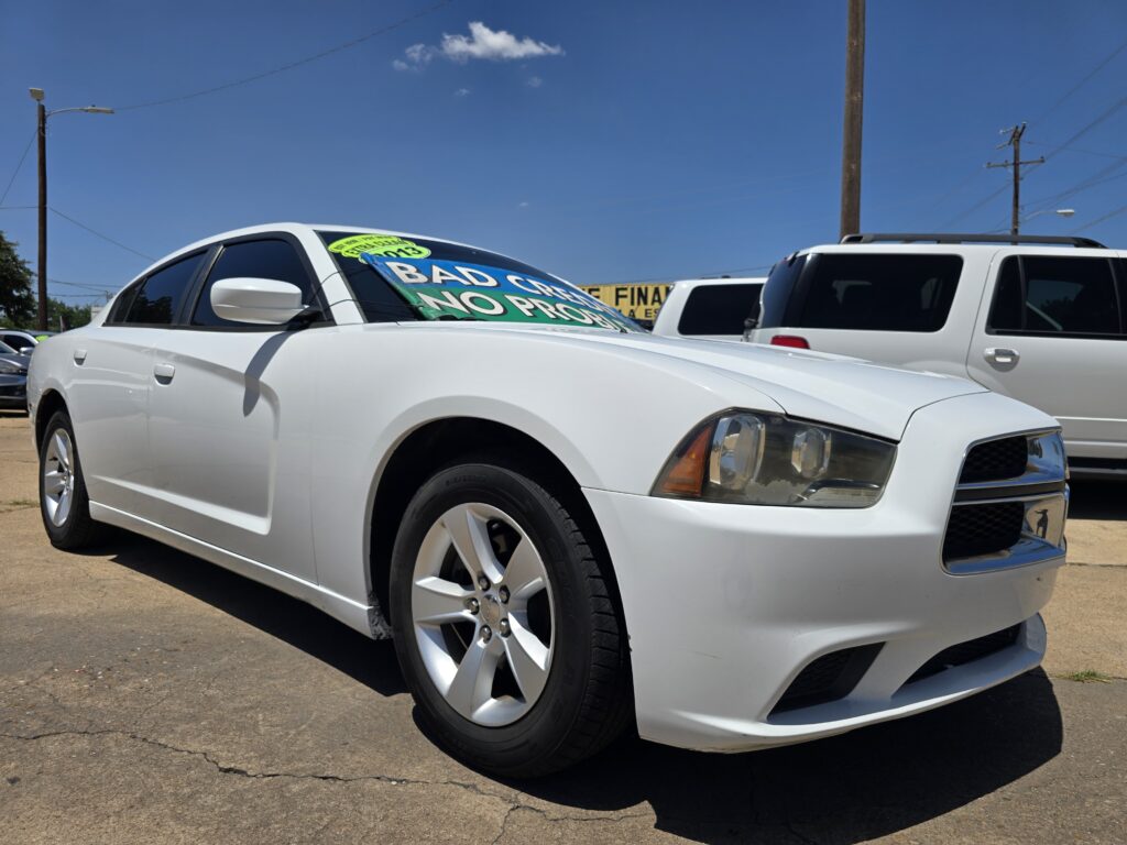 White sedan in a parking lot with a large green and blue windshield sign advertising financing or specials, partially obscuring the windshield view of the car's interior.