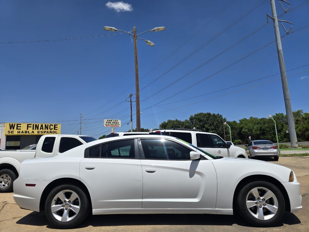 White car in the foreground at a used car lot with a bright yellow 'WE FINANCE' sign and clear blue sky.
