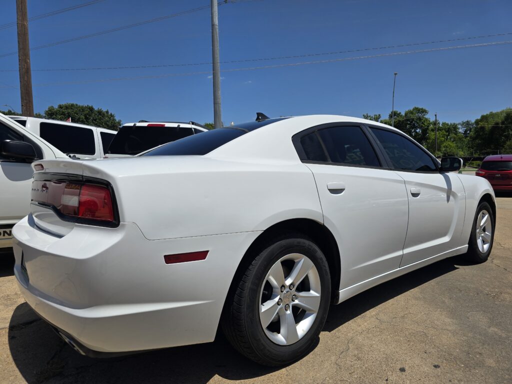 White Dodge Charger in a parking lot with other cars, blue sky and utility poles overhead.