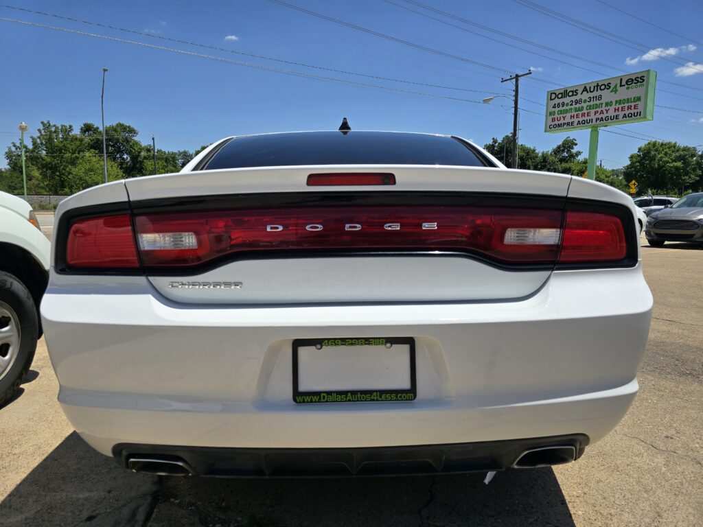 Rear view of a white Dodge Charger with a Dallas Autos 4 Less sign in the background.