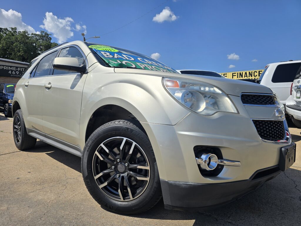 Silver SUV parked at a dealership with bold green sale signage on the windshield and a yellow finance banner in the background under a blue sky.