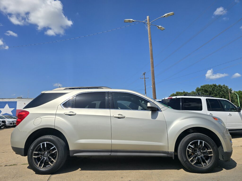 Large silver SUV parked in a lot under a blue sky with a wooden utility pole and streetlights overhead.