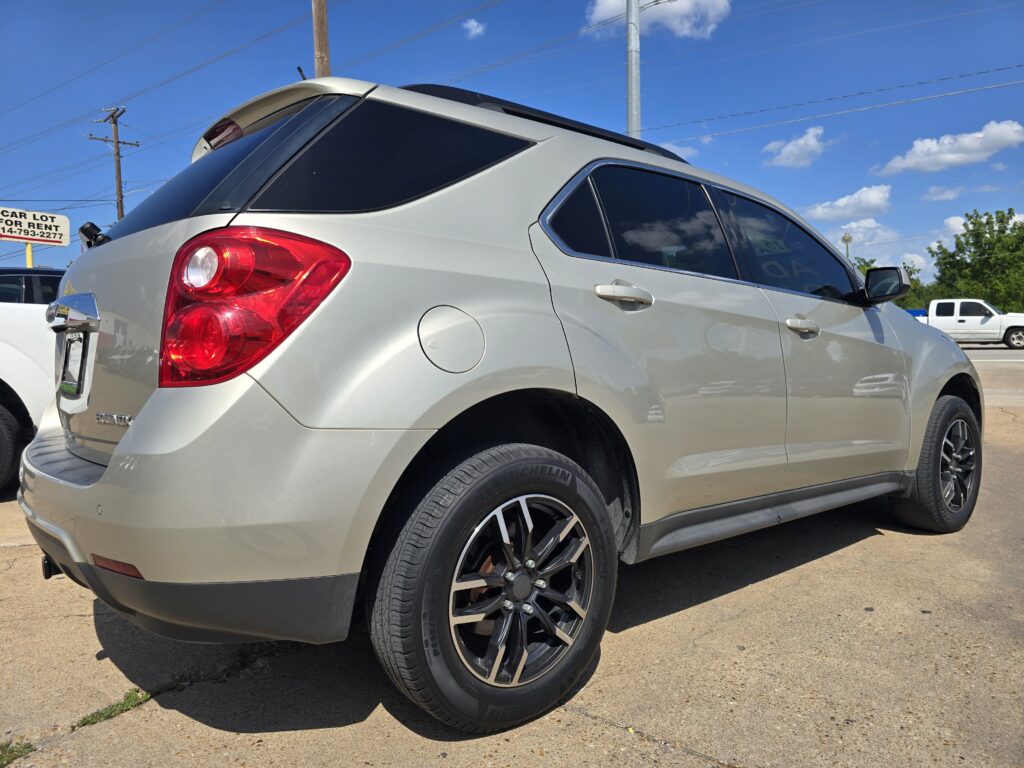 Silver SUV from the rear left side in a parking lot on a sunny day with a blue sky and white clouds.