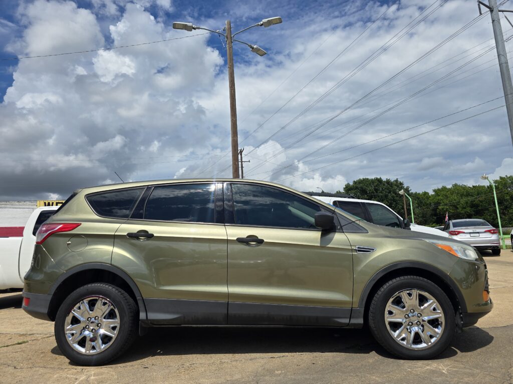 Gold SUV parked in a car lot, other vehicles visible, under a blue sky with clouds and power lines overhead.