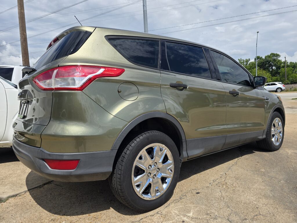 Rear-left quarter of a metallic gray SUV in a parking lot, showing the taillight, rear window, and chrome wheels.