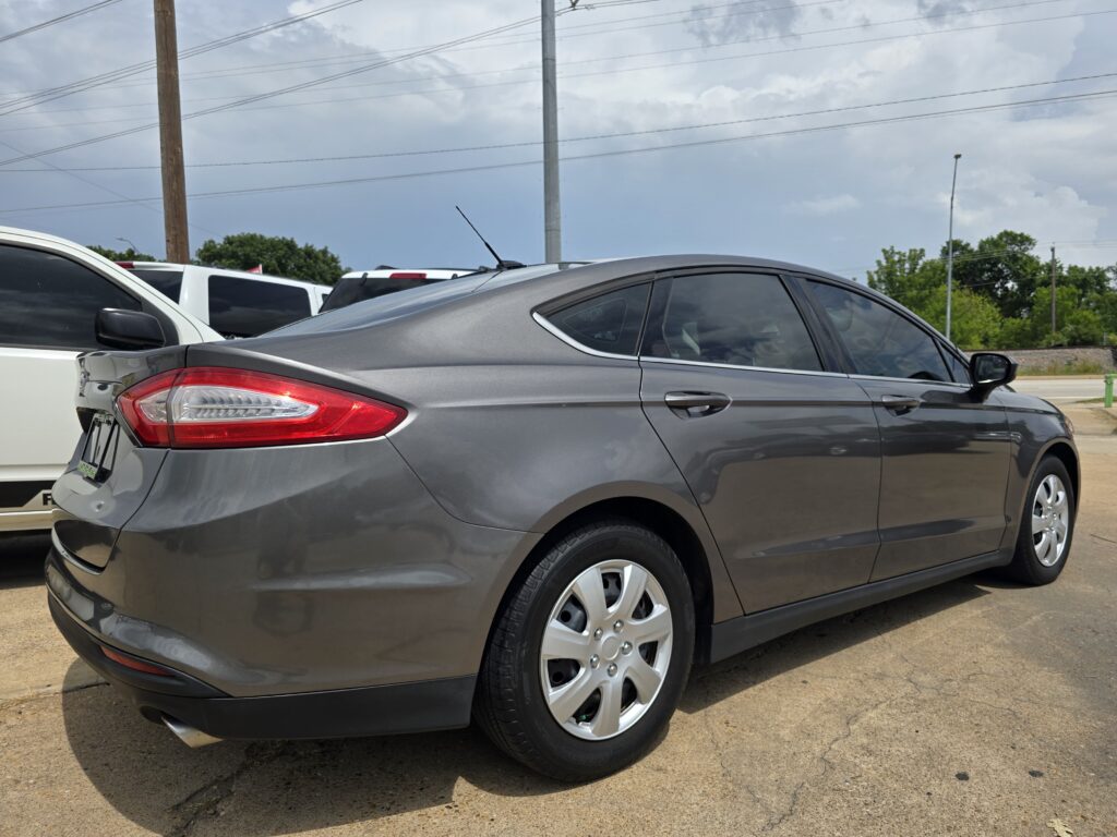 Rear-right view of a gray sedan in a parking lot, with a white SUV beside and power lines overhead.