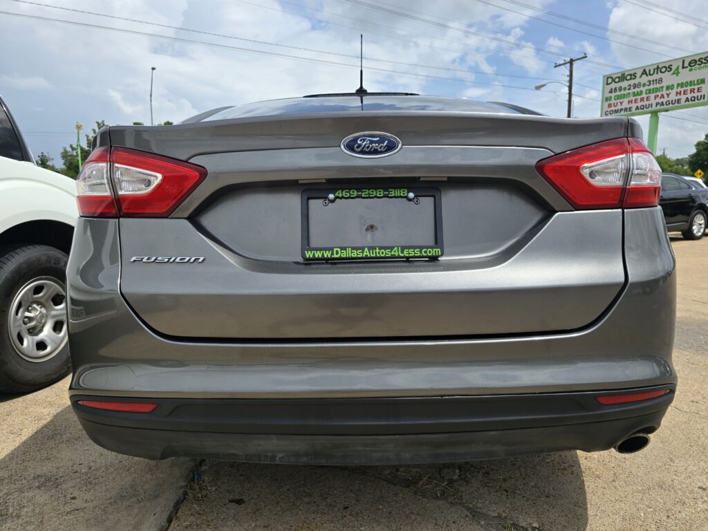 Rear view of a gray Ford Fusion in a parking lot with a dealership sign in the background