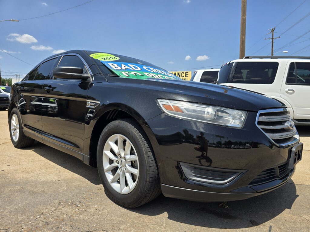 Black SUV at a dealership with a bright yellow/green 'Bad Credit' sign taped to the windshield and a 2013 sticker visible on the glass.