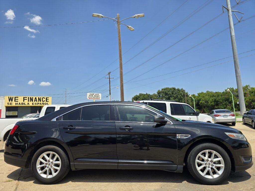 Black SUV in a dealership lot with a yellow 'WE FINANCE' sign in the background and clear blue sky.
