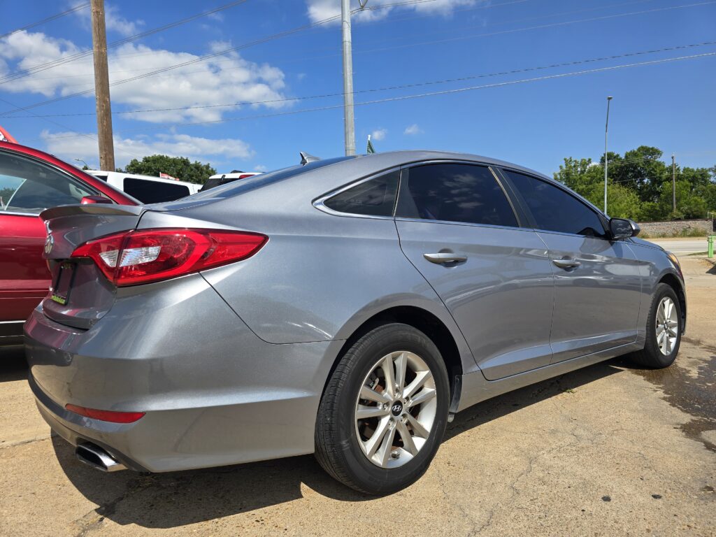 Rear and side view of a silver sedan parked next to a red car on a sunny day with utility poles and blue sky in the background.