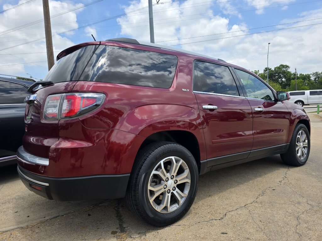 Maroon GMC SUV parked in a lot, showing rear and side panels with a reflected cloudy sky in the windows (SLT badge visible).