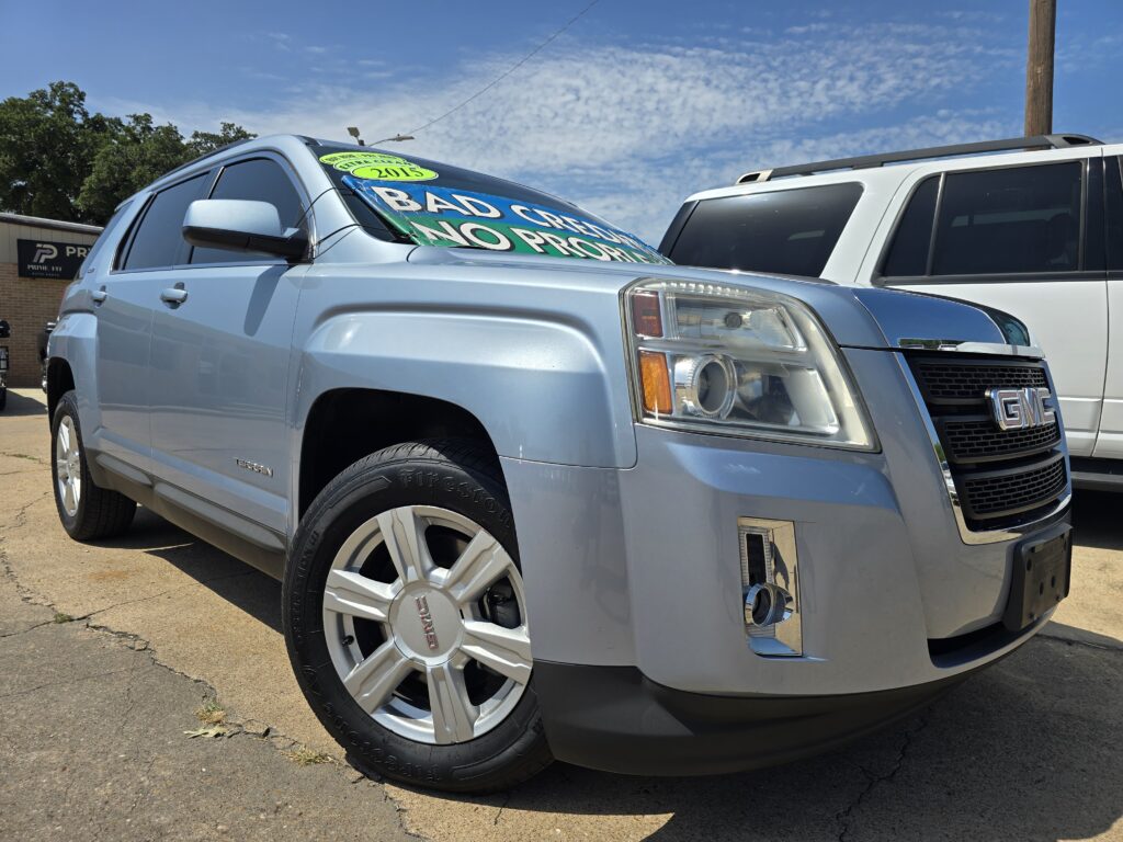 Blue GMC SUV in a parking lot with a bold windshield sign reading 'BAD CREDIT' in bright green letters, parked beside a white SUV against a clear blue sky.