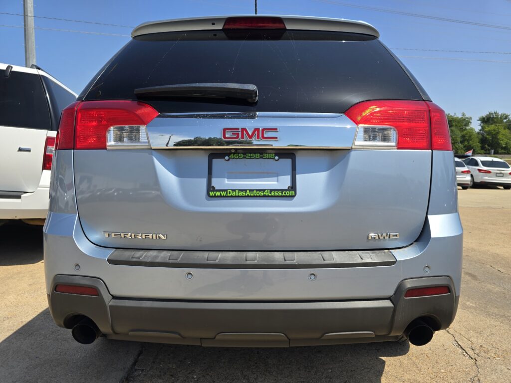 Rear view of a gray GMC Terrain SUV with AWD and a DallasAutos4Less dealership plate frame on a sunny lot.