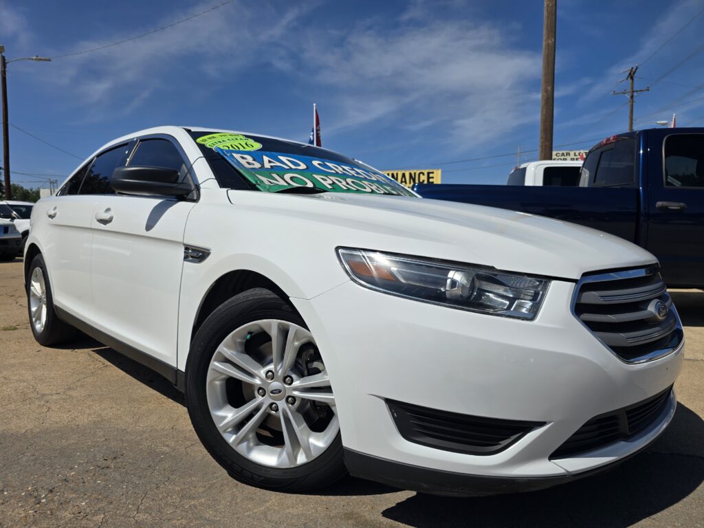 White SUV at a car dealership with bold green windshield signs reading 'BAD CREDIT NO PROBLEM' and a blue '2016' sticker, under a clear blue sky.
