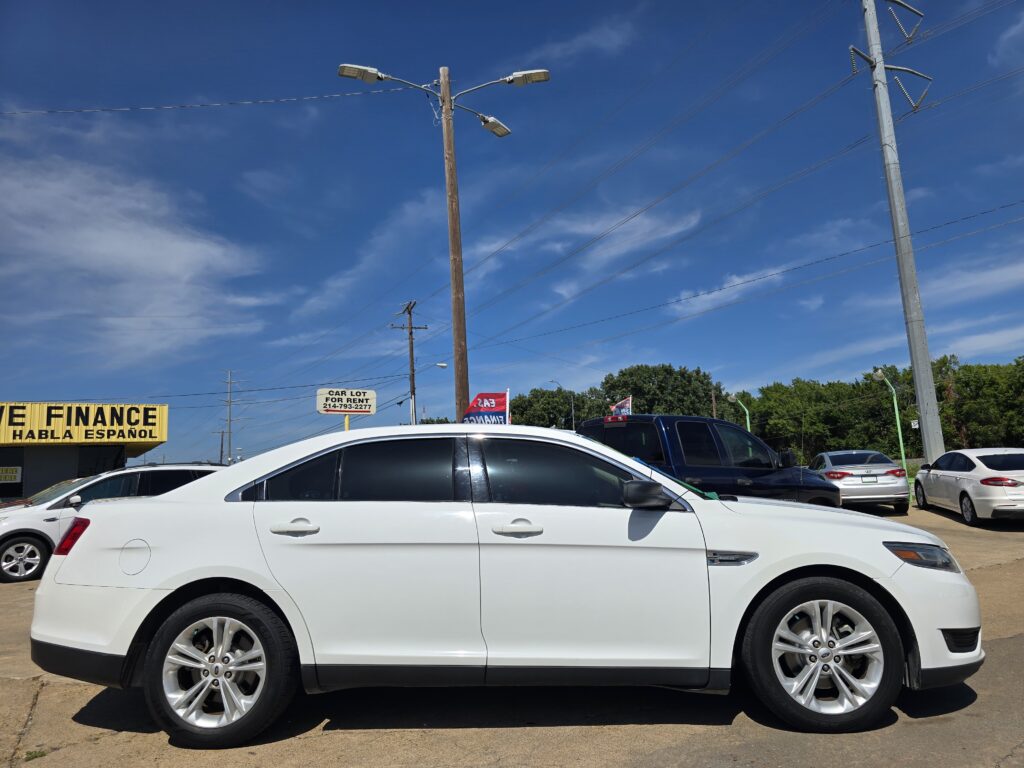 White SUV in a car dealership lot with a yellow finance sign and other vehicles under a blue sky.